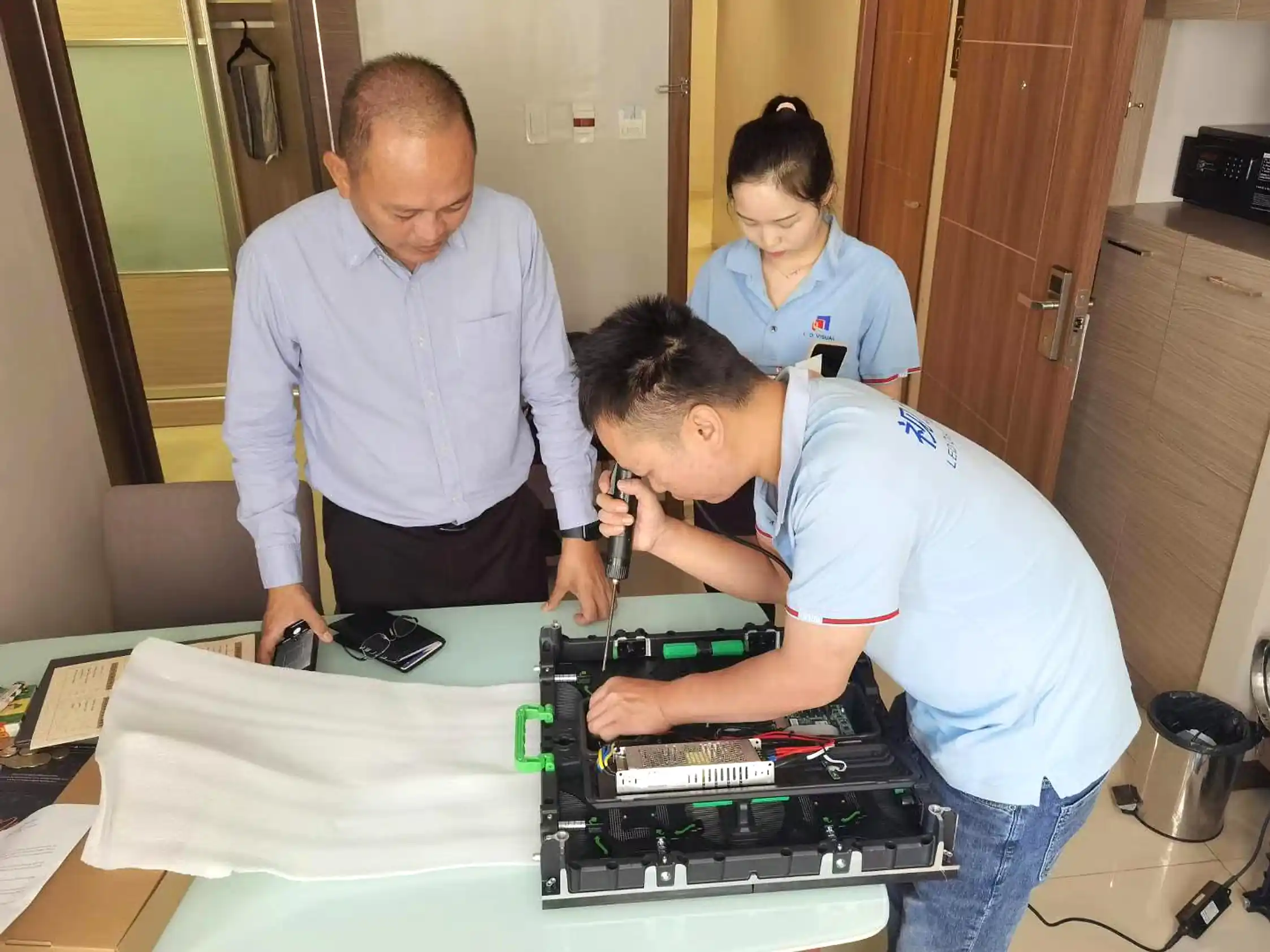 LED display importer and factory engineer reviewing LED modules, receiving cards, power supplies, and connectors on an inspection table